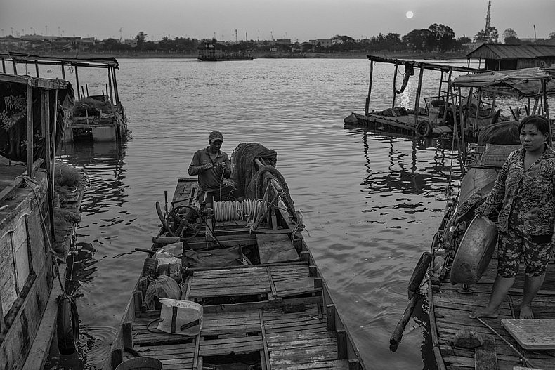 Bich, a professional fisherman, repairs wires in his boat's engine before heading onto the river to fish. Photo by Gareth Bright.