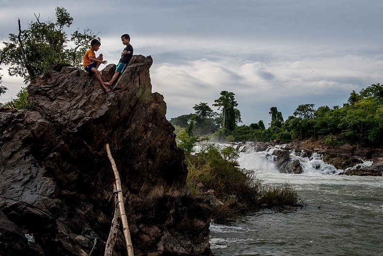 The young sons of a fisherman sit on the banks of the Mekong below the Khone Phapheng waterfalls, waiting for their father to return from his afternoon fishing. Photo by Luc Forsyth.