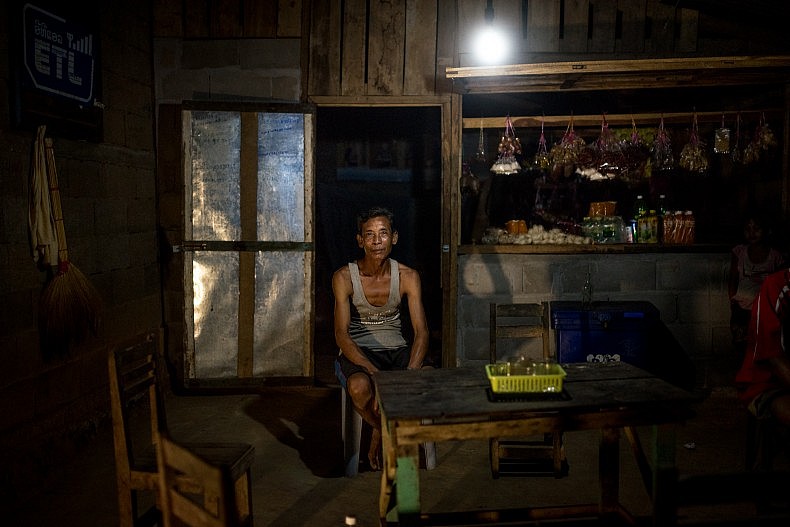 Xieng Pai, 54, is a shopkeeper in the village of Khoc Kham. He powers the light in his shop using a portable water turbine. Photo by Luc Forsyth.